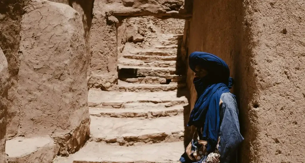 Einheimischer Berber mit blauem Turban geht durch eine enge Steingasse in Aït Benhaddou