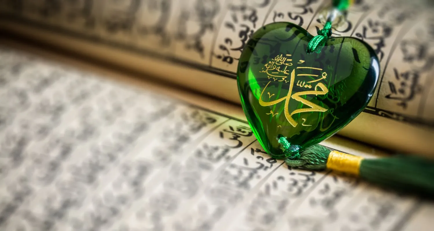 Green pendant with the Prophet's name in gold calligraphy resting on an open Ǫuran